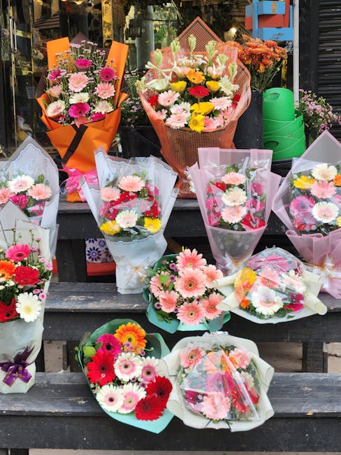 A display of various fresh floral bouquets arranged on rustic wooden steps outside a flower shop. The bouquets feature a mix of flowers including pink and white daisies, gerbera daisies, and carnation